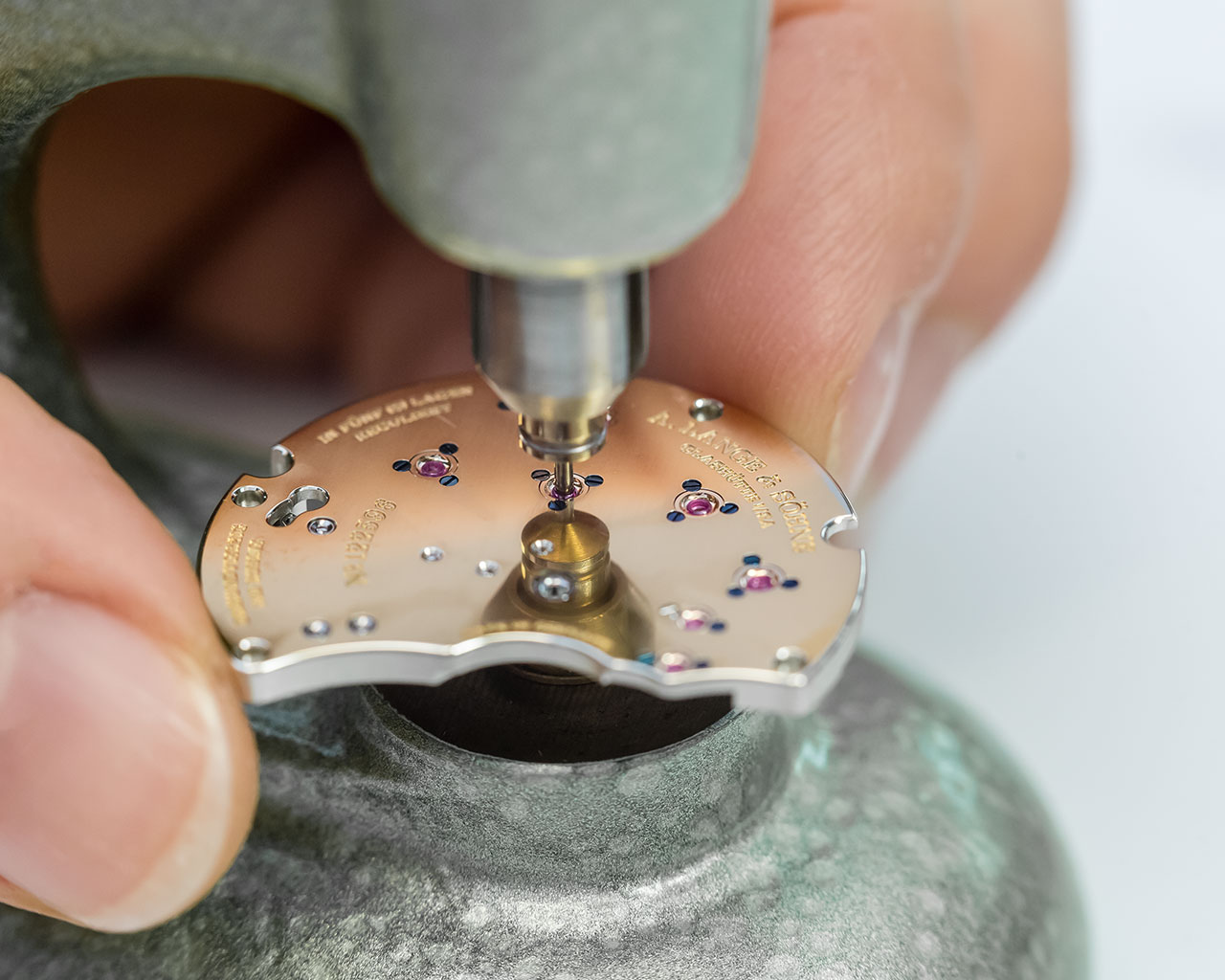 The bearing jewels are pressed into the bores by hand. The friction is reduced by adding a droplet of oil in the recesses of the synthetic ruby bearings. 